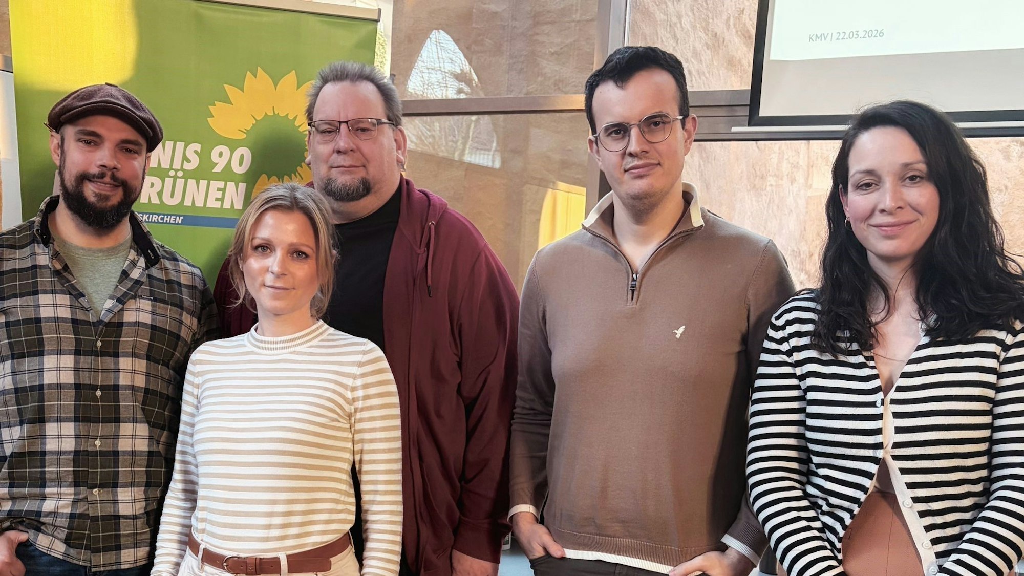 Drei Männer und zwei Frauen stehen vor einem Plakat der Grünen.