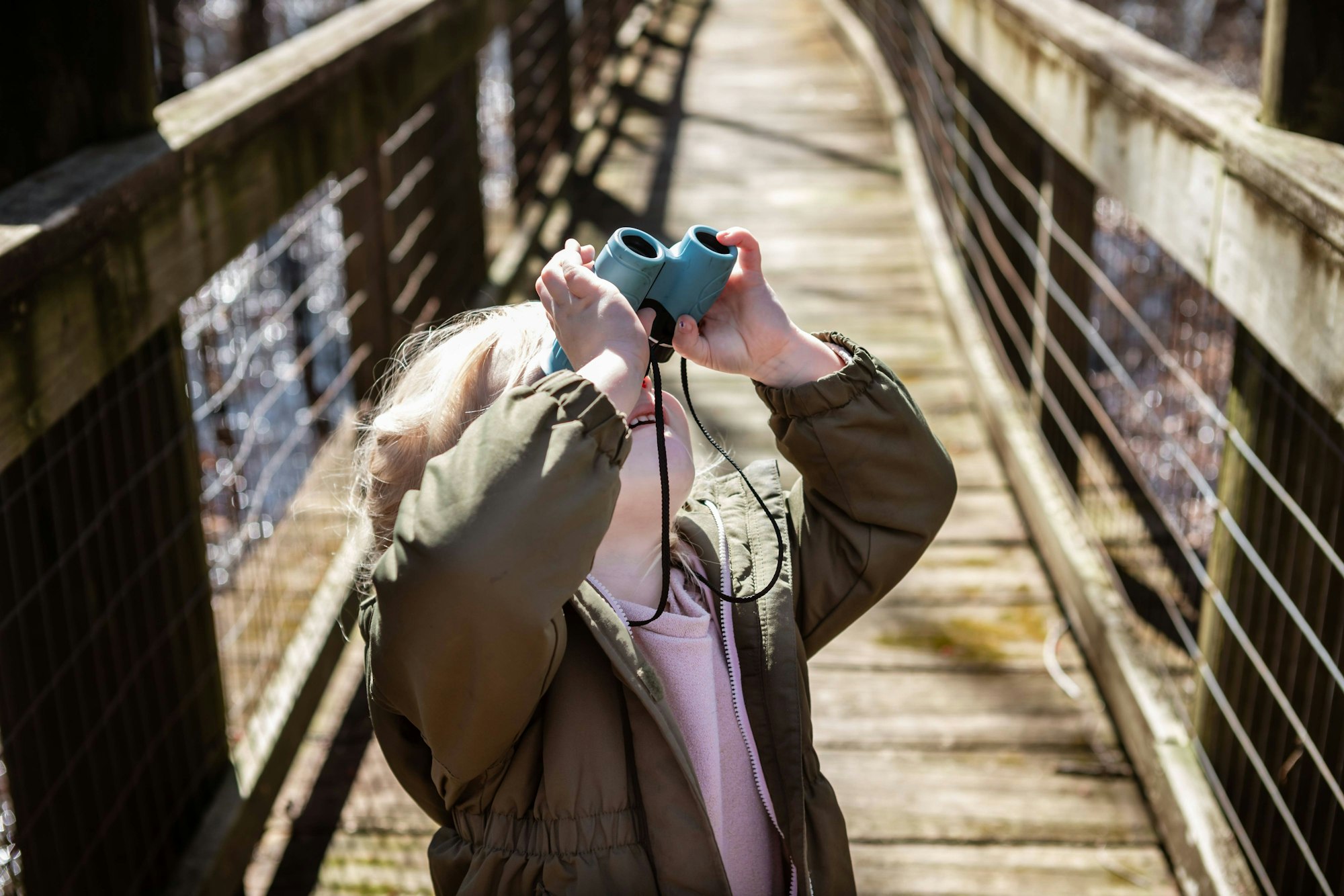 Ein kleines Mädchen steht auf einer Brücke und beobachtet mit einem kleinen Fernglas den Himmel.