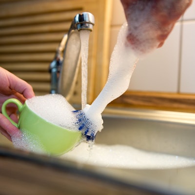 Viel Schaum beim Spülen einer Tasse im Spülbecken.