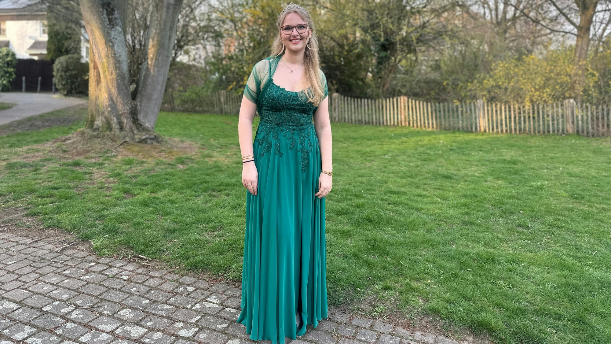Maikönigin Emma Klaassen trägt ein grünes Ballkleid und steht am Rand einer Wiese.