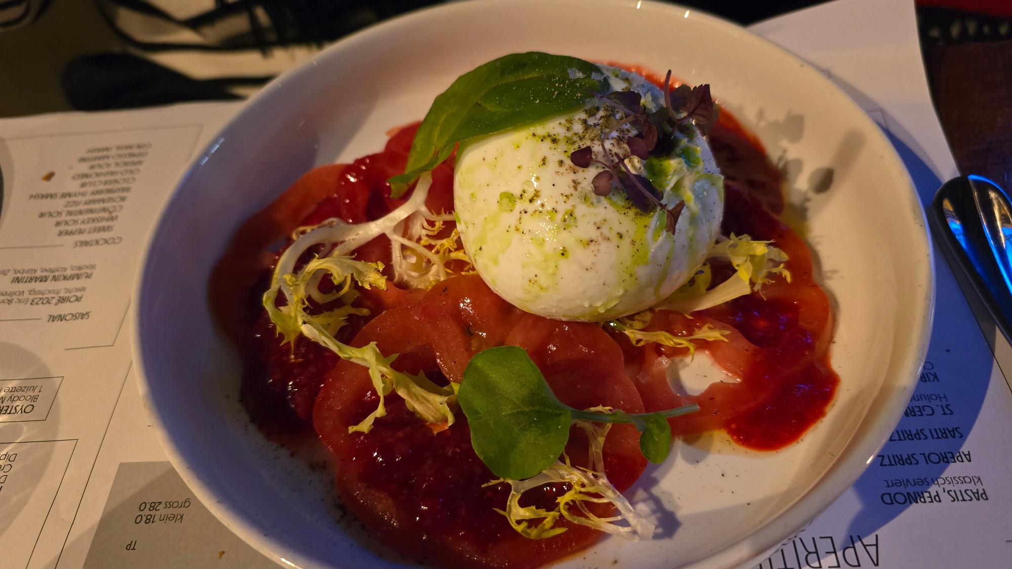 Burrata als weiße Kugel sitzt auf großen Tomatenscheiben