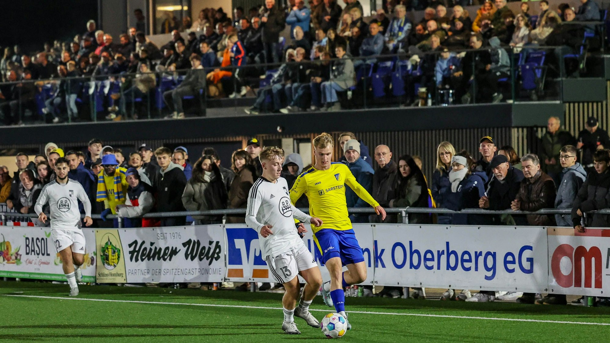 Vor voller Tribüne laufen ein Wiehler und ein Nümbrechter Fußballer um den Ball.