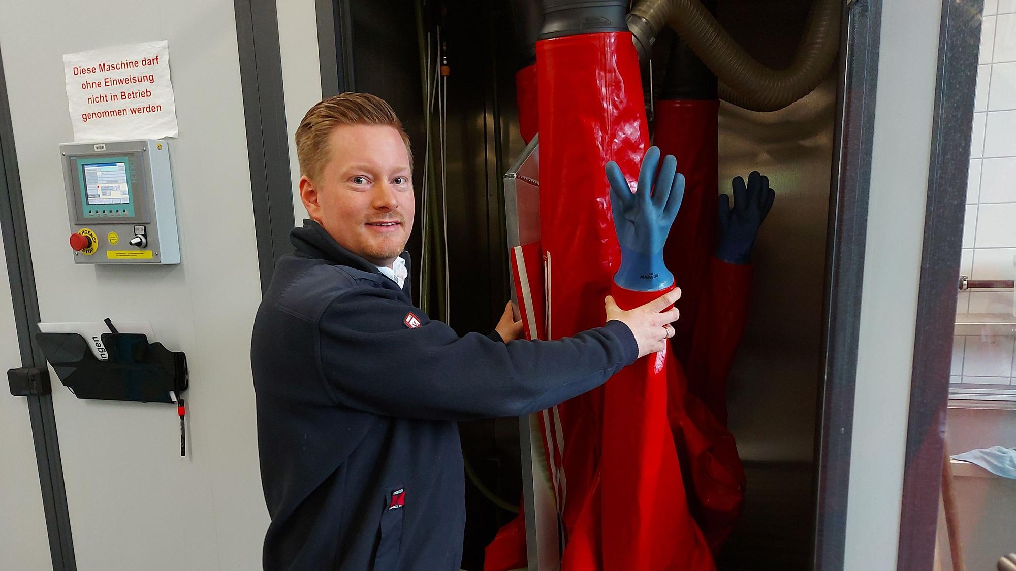 Ein Mann hält einen roten Schutzanzug der Feuerwehr in eine Dusche.