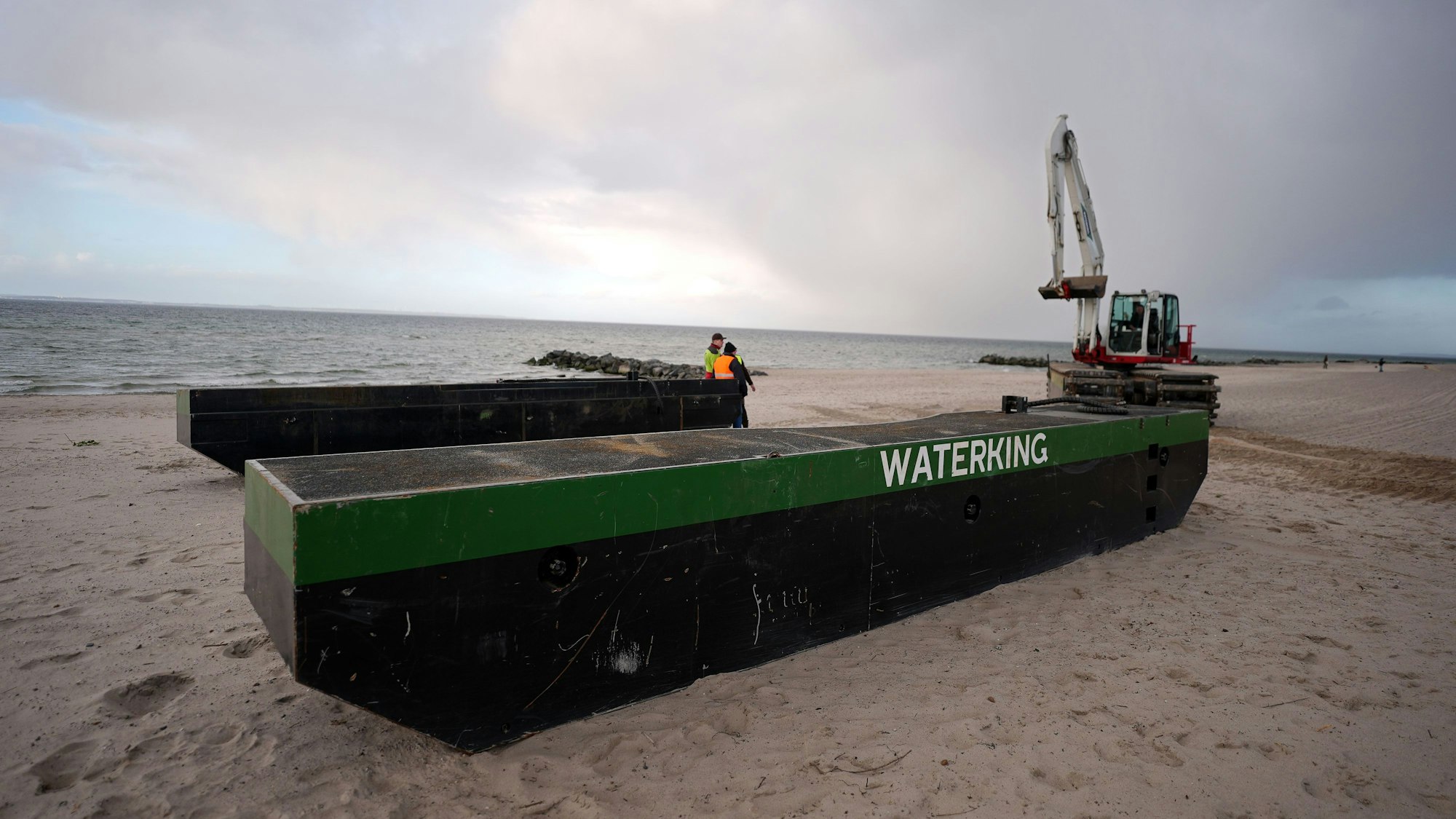 Ein Spezial-Schwimmbagger (r) wird neben Schwimmpontons an den Strand bei Niendorf gefahren, wo ein Wal im flachen Wasser gestrandet ist.