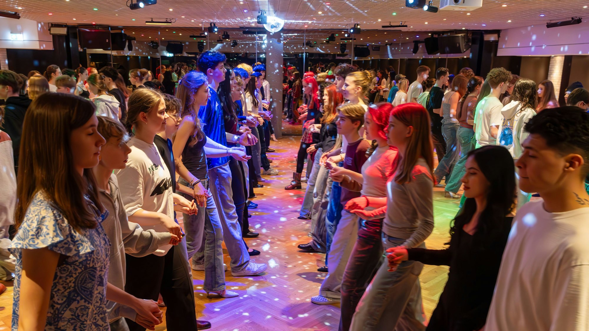 Die Fledermausquadrille wird in der Tanzschule van Hasselt geprobt, in der Mitte der linken Seite tanzen Emilia und Joscha. In dem Saal mit der Discobeleuchtung werden auch Partys gefeiert.