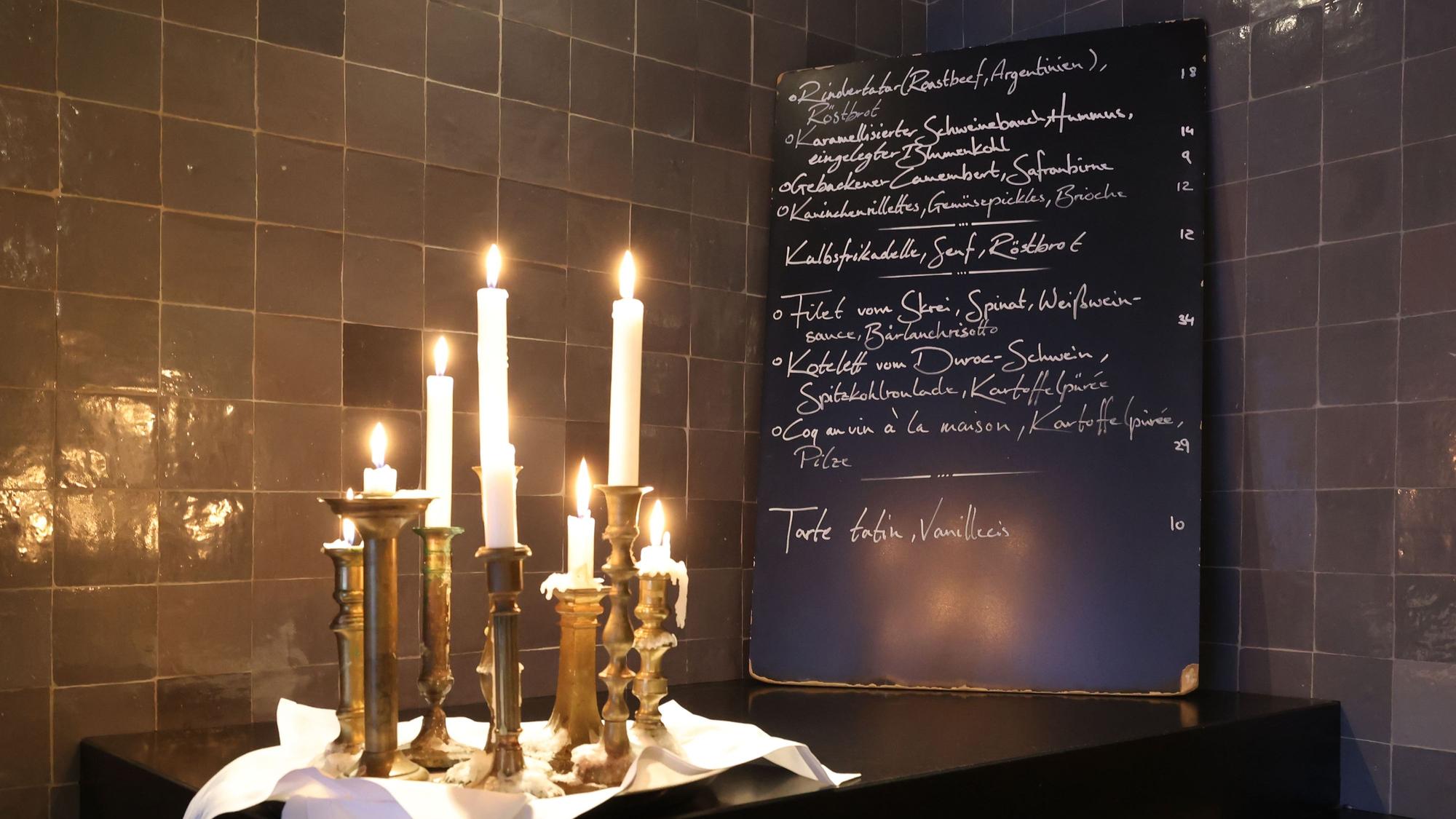 Eine handbeschriebene Tafel ist zu sehen, davor brennende Kerzen.