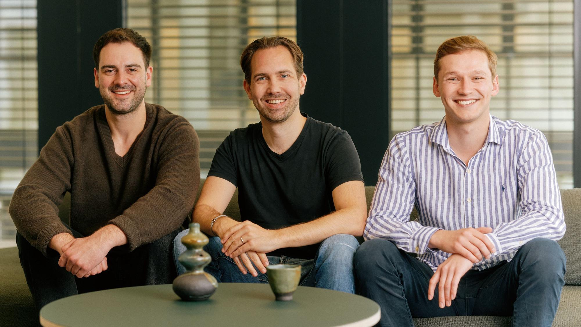 Lars Möhring, Markus Musiol und Albert Schwarzmeier sitzen auf einem Sofa und lächeln in die Kamera.