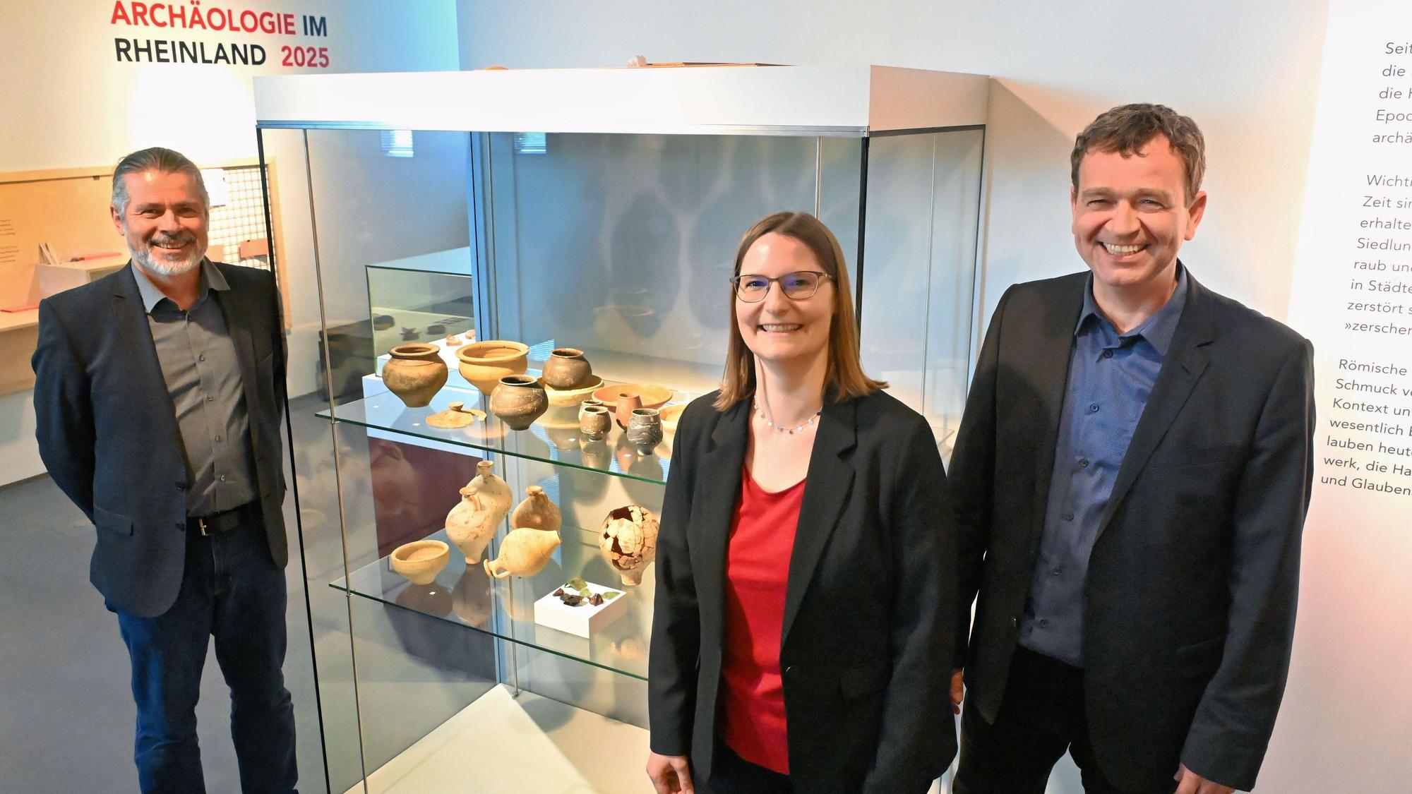 Zwei Frauen und ein Mann stehen an einer Vitrine der neuen Ausstellung in den Römerthermen in Zülpich.