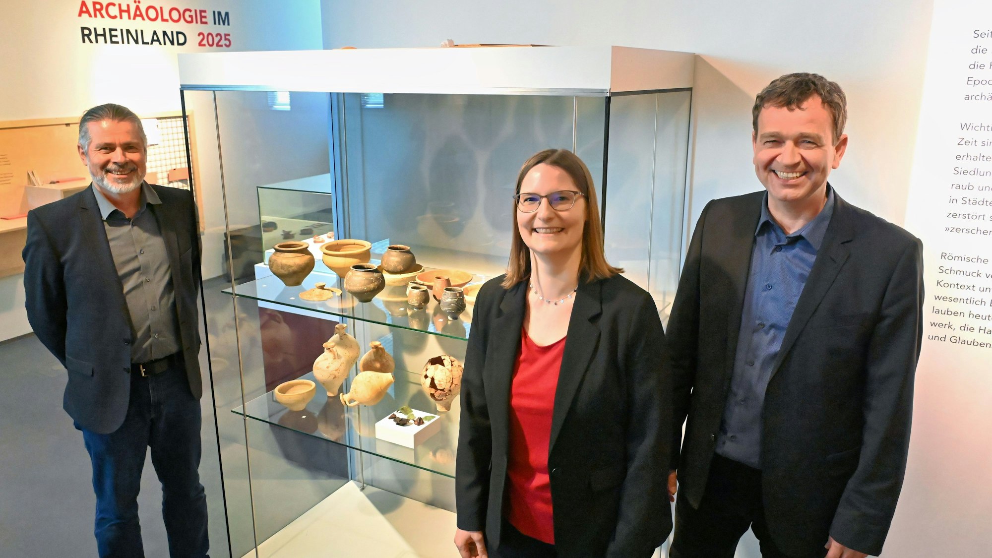 Zwei Frauen und ein Mann stehen an einer Vitrine der neuen Ausstellung in den Römerthermen in Zülpich.