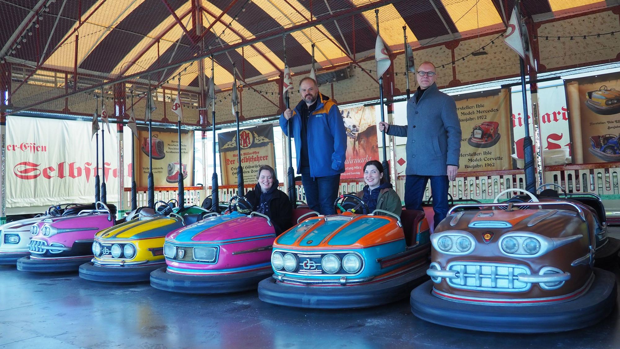 Die bunten kleinen Autos stehen in einer Reihe, Daniel Manner und Carsten Vorwig stehen hinten und halten sich an der Stange des Stromabnehmers fest, Anne Carl und Margarethe Becker sitzen in zwei Scootern.