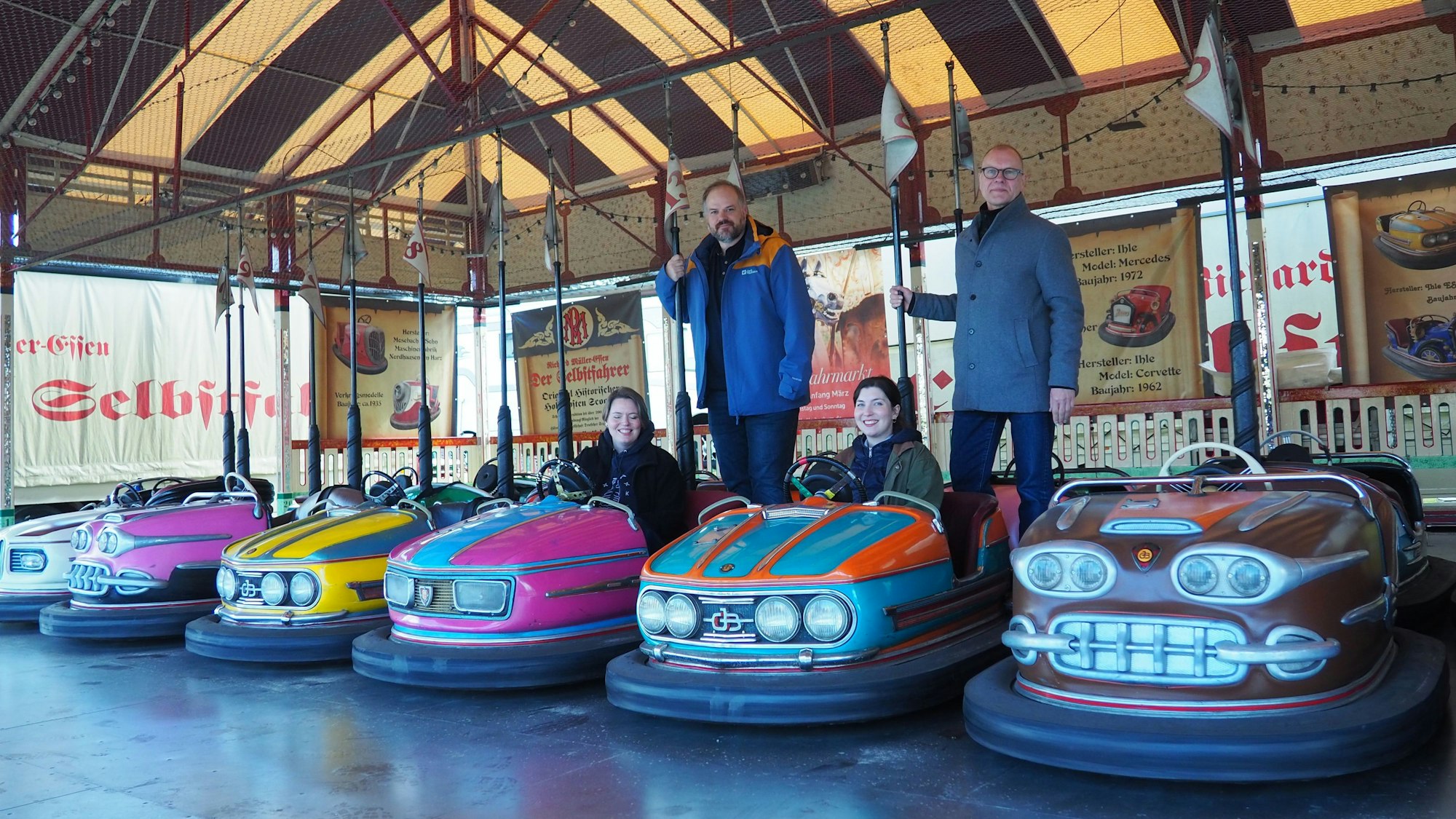 Die bunten kleinen Autos stehen in einer Reihe, Daniel Manner und Carsten Vorwig stehen hinten und halten sich an der Stange des Stromabnehmers fest, Anne Carl und Margarethe Becker sitzen in zwei Scootern.