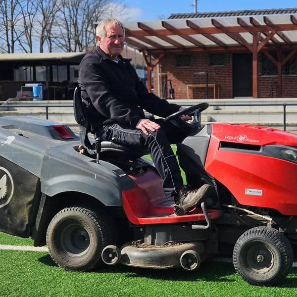 Ein Mann sitzt auf einem Minitraktor auf einem Sportplatz.