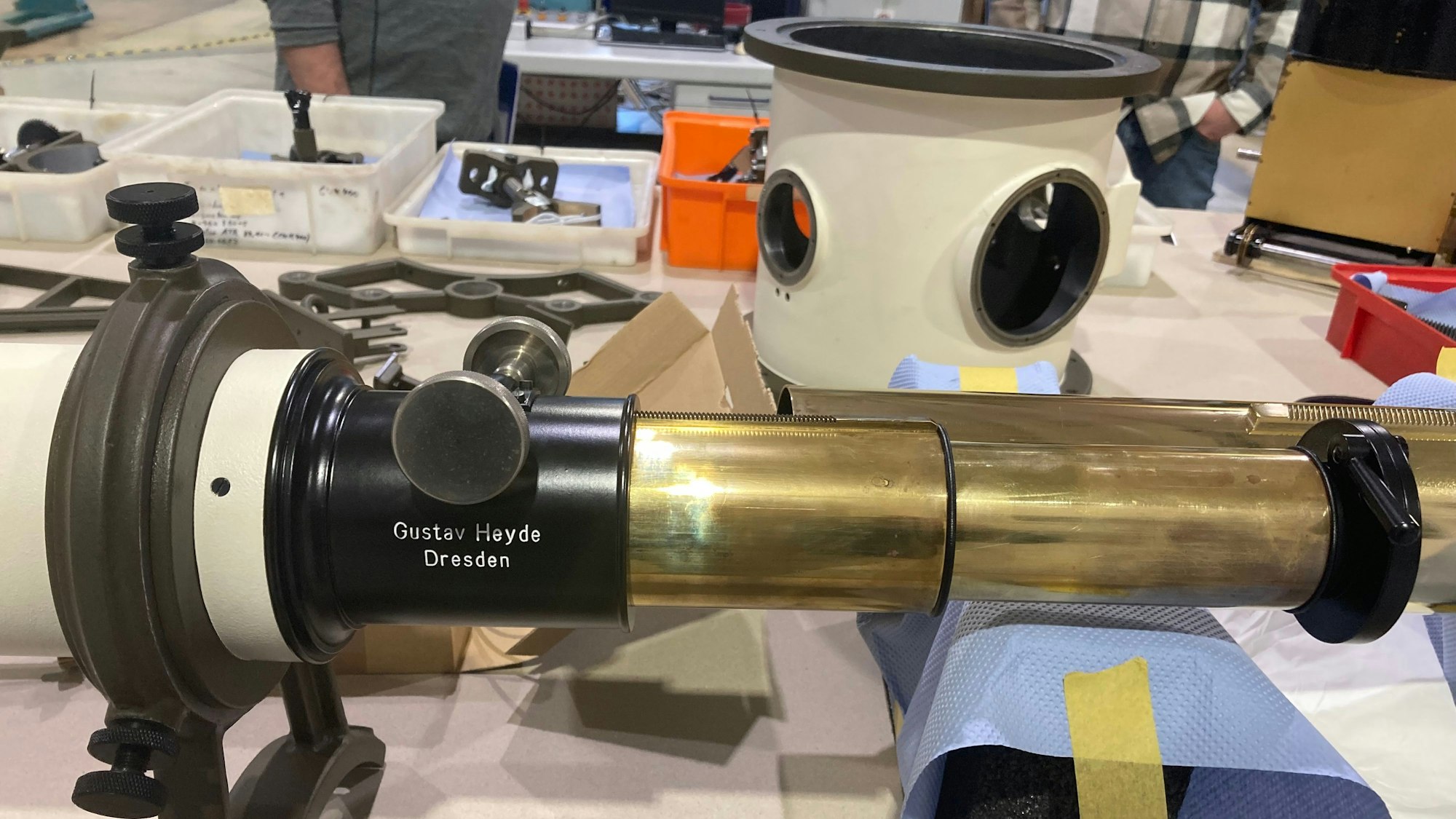 Auf einem Tisch liegt ein Fernrohr, im Hintergrund stehen Schalen mit Teilen.