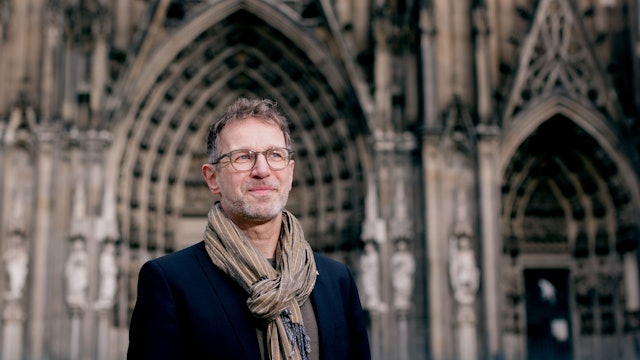 Ein Mann steht vor einer Kirche und blickt in die Ferne.