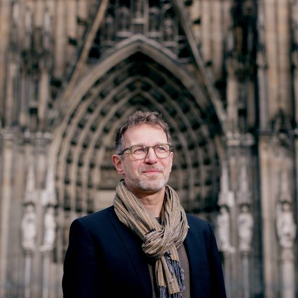 Ein Mann steht vor einer Kirche und blickt in die Ferne.