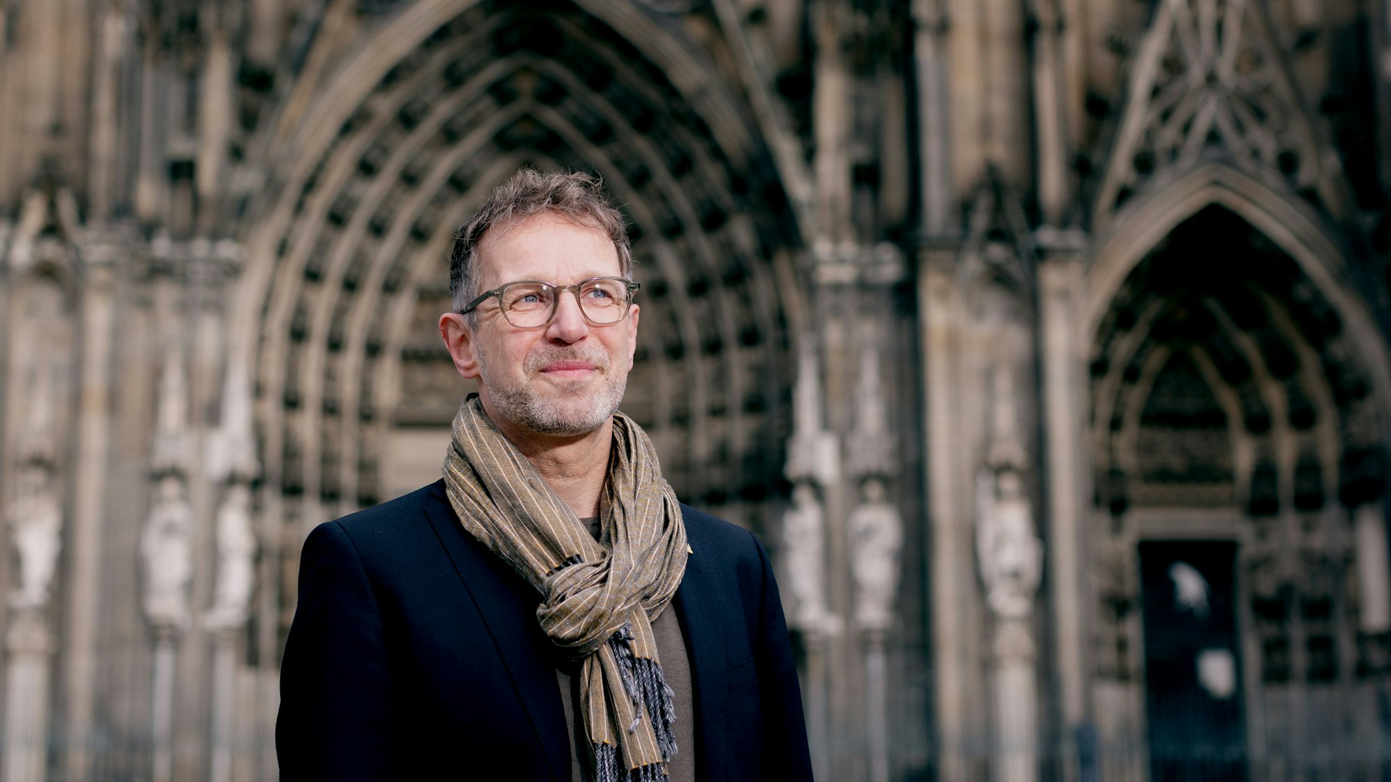 Ein Mann steht vor einer Kirche und blickt in die Ferne.