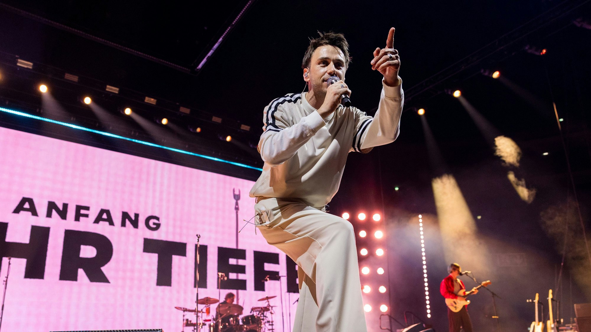 Ein Mann steht auf einer Bühne, hält ein Mikrofon in der rechten Hand und singt.