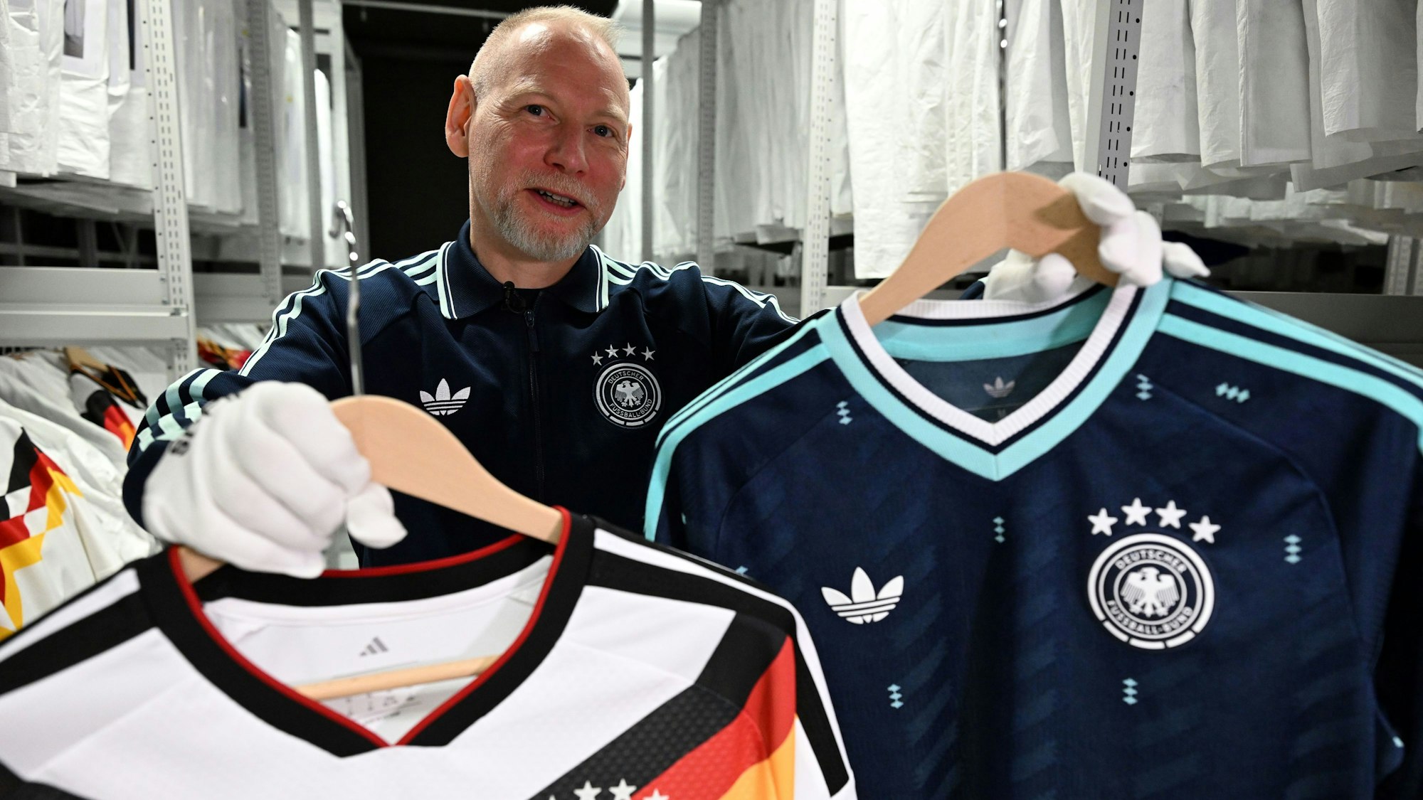 Designer Jürgen Rank hält Trikots der Nationalmannschaft in den Händen, die er gestaltet hat.