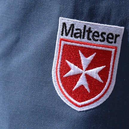 Das Logo der Malteser ist an der Jacke eines Helfers zu sehen.
