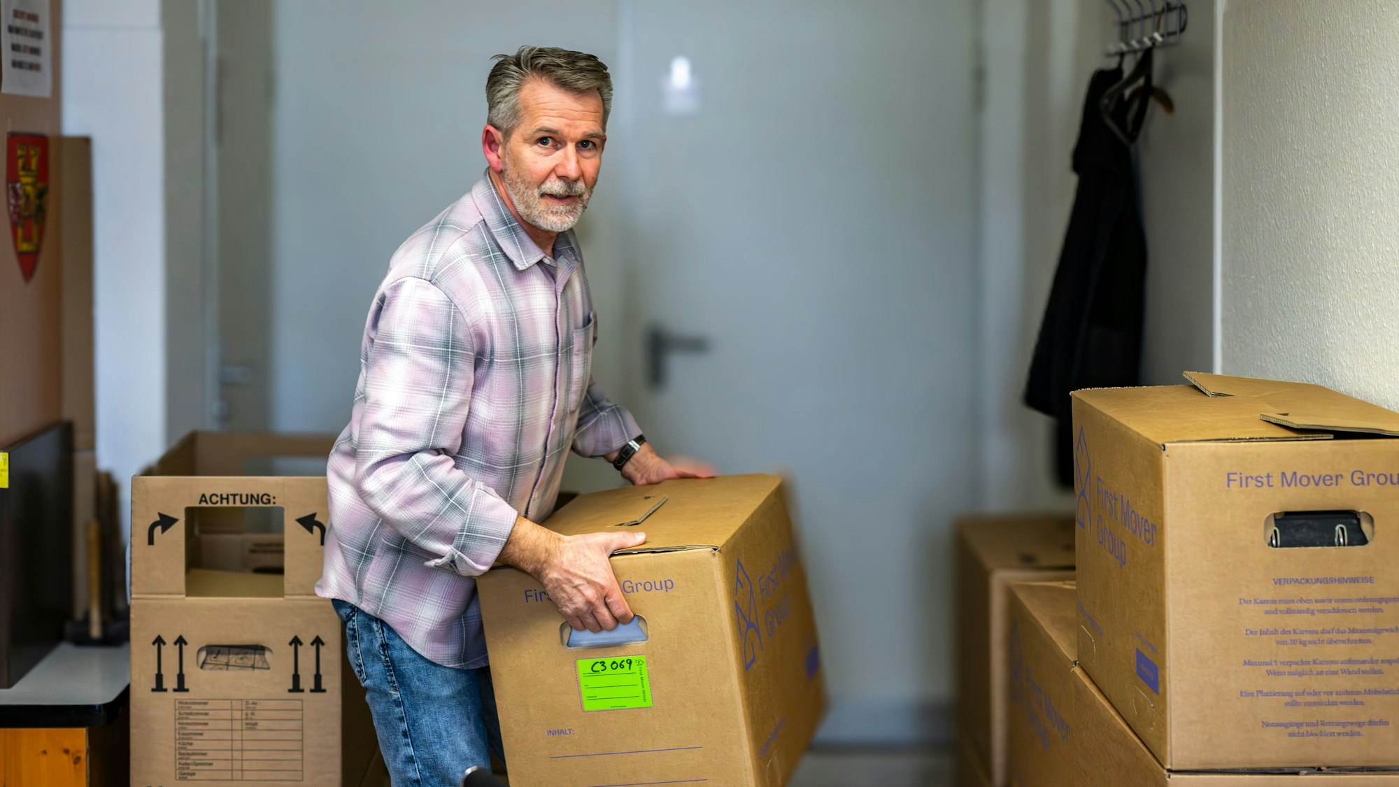 Ein Mann trägt einen Umzugskarton. Weitere Kartons stehen um ihn herum.