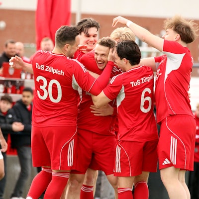 Freudestrahlend steckt Thoma Leßenich inmitten seiner Spieler, die ihm zum Freistoßtor gratulieren.