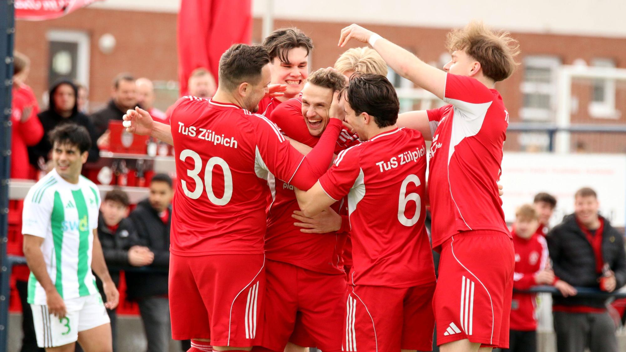Freudestrahlend steckt Thoma Leßenich inmitten seiner Spieler, die ihm zum Freistoßtor gratulieren.