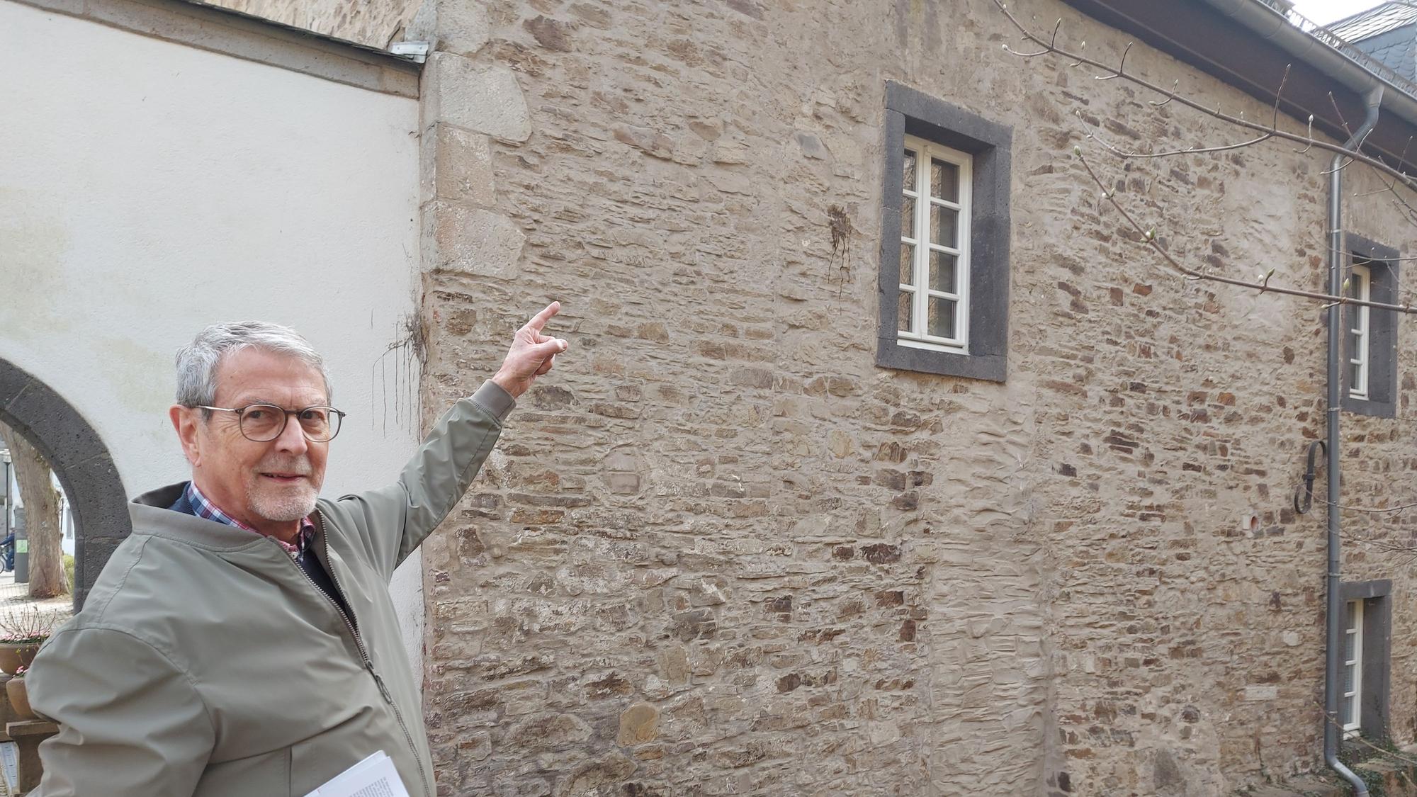 Ein Mann steht vor einem Bruchsteingebäude und zeigt auf ein Fenster.