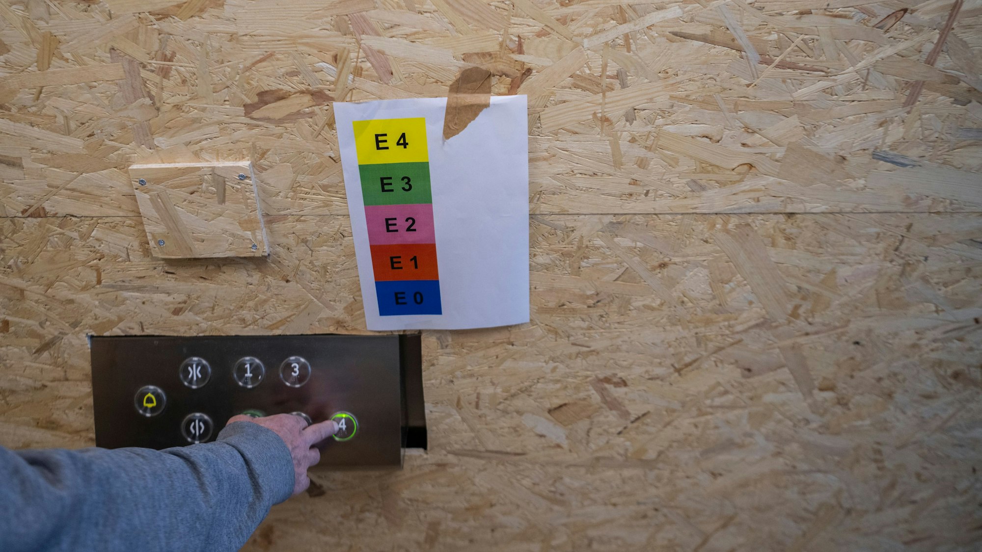 An einer Holzwand hängt ein Zettel mit Abkürzungen wie E4 in fünf verschiedenen Farben.