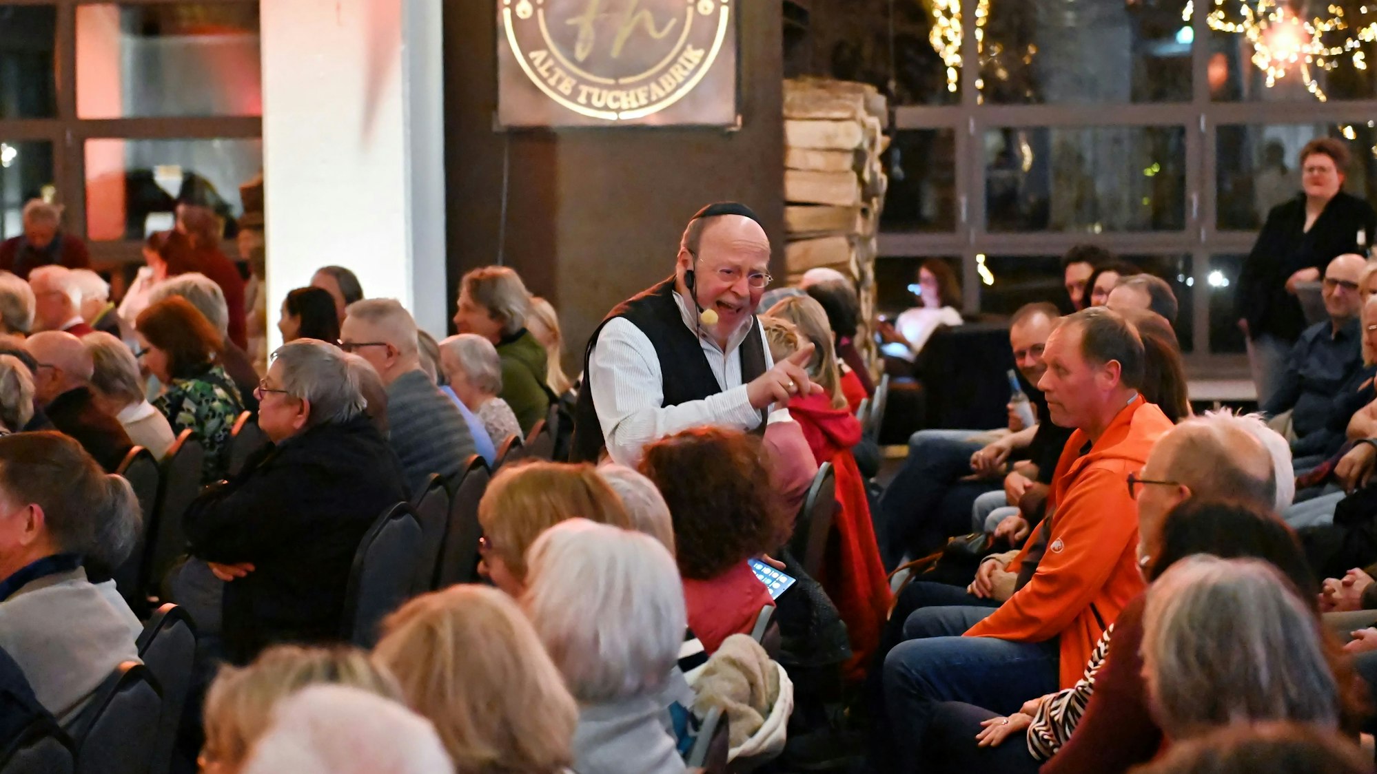 Ein Mann mit einem Mikrofon am Mund spricht mit dem Publikum.