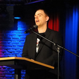 Ein Mann steht an einem Pult und spricht in ein Mikrofon.