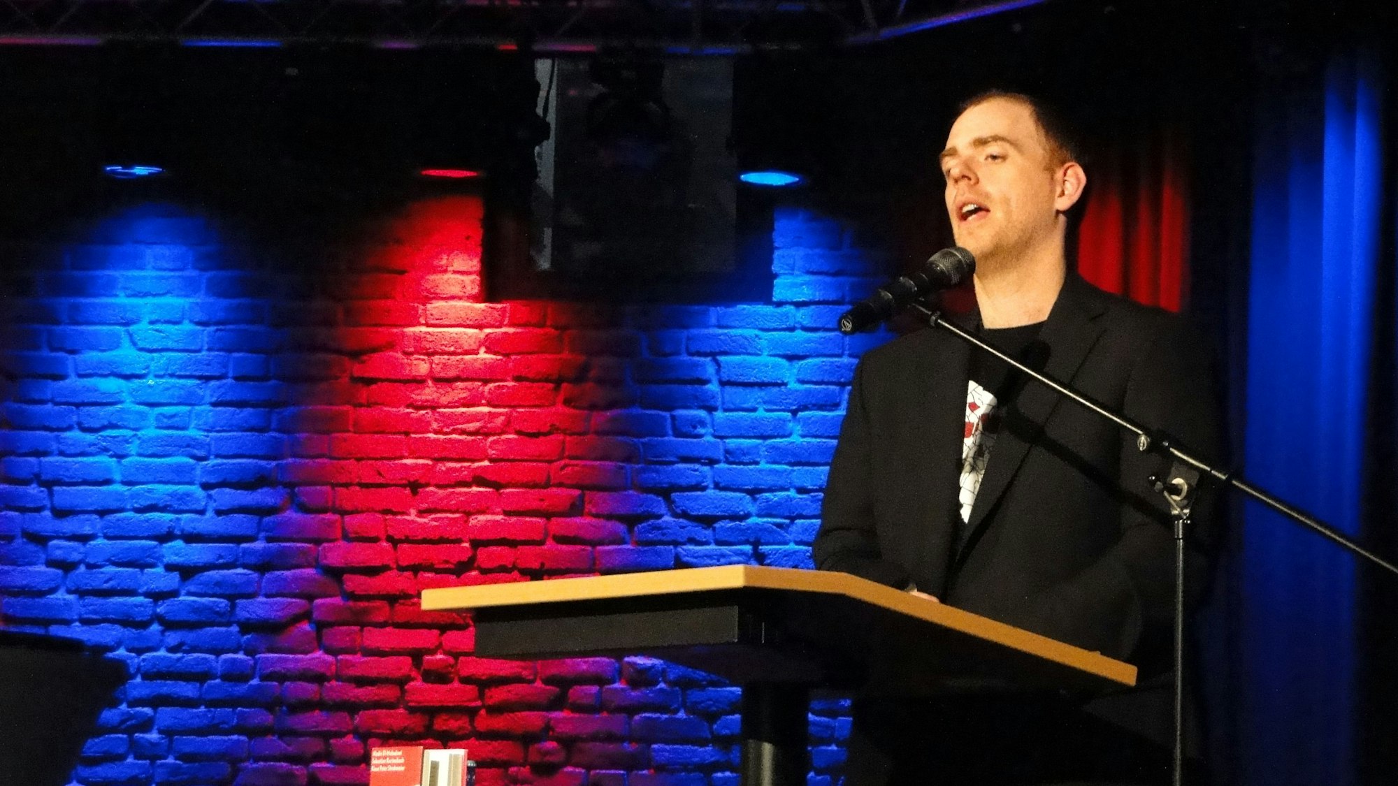 Ein Mann steht an einem Pult und spricht in ein Mikrofon.