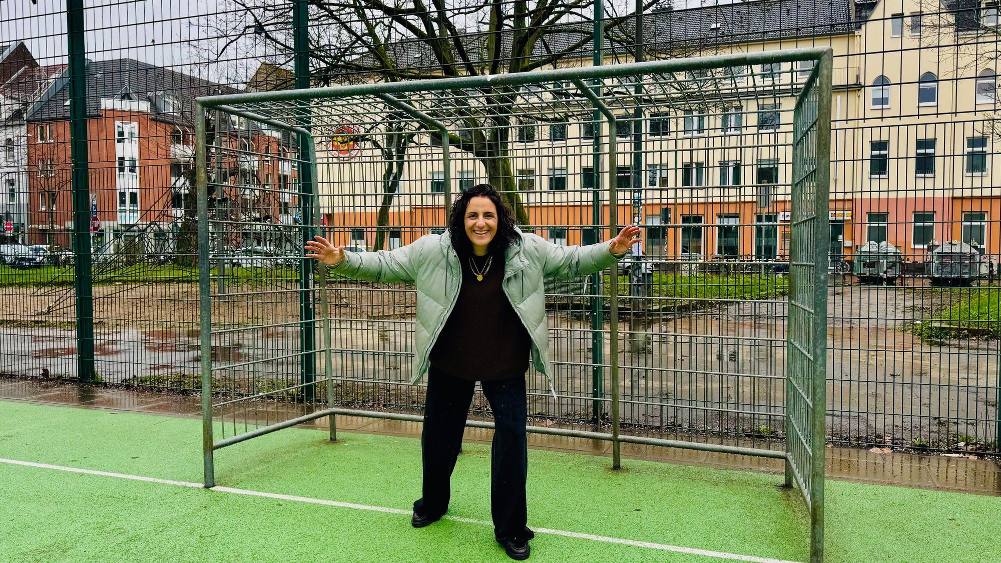 Eine Frau steht vor einem Fußballtor auf einem Bolzplatz.