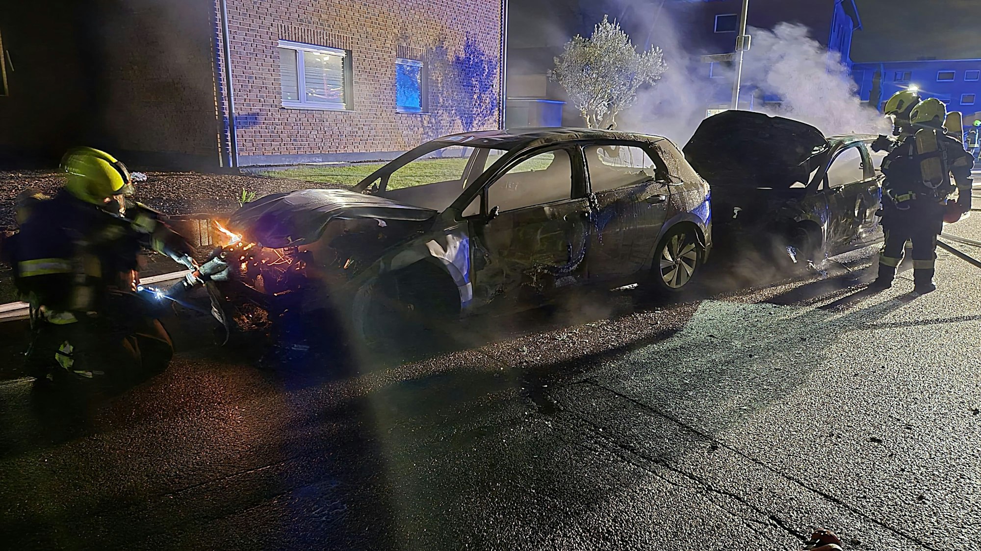 Feuerwehrleute stehen vor ausgebrannten Autos.