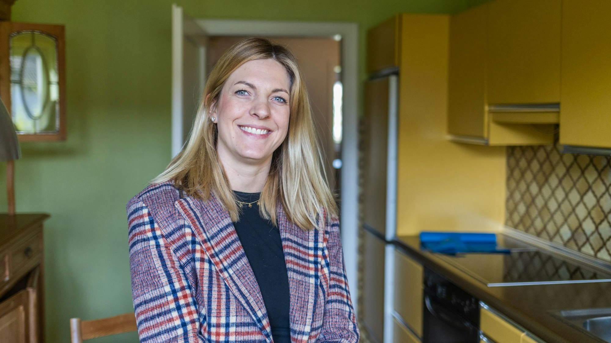 Eine blonde Frau im Blazer lächelt in die Kamera.