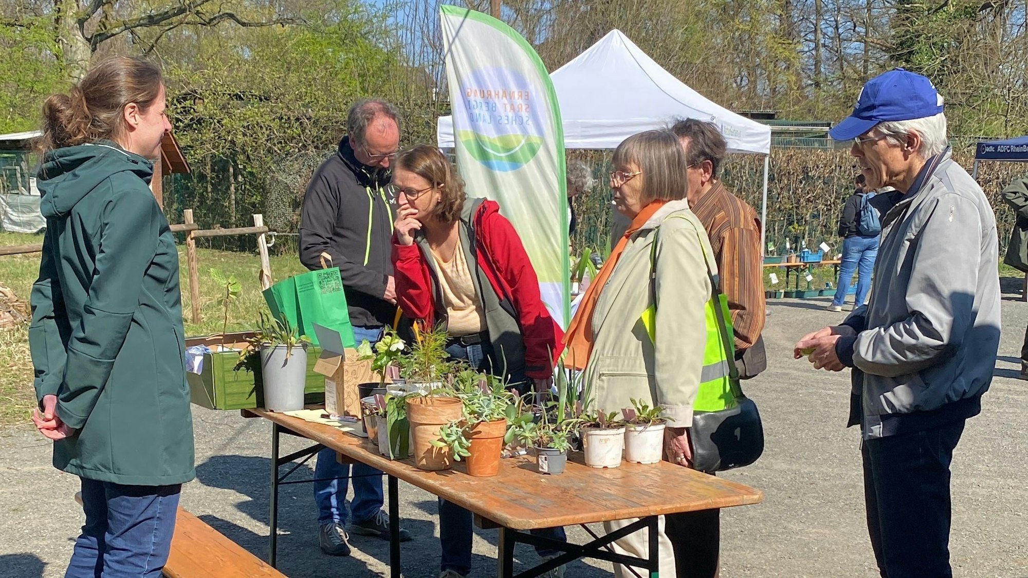 Sechs Personen stehen um einen Tisch herum, auf dem verschiedene Pflanzen stehen.