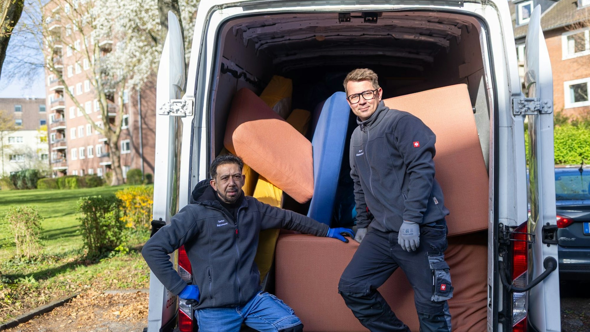 Zwei Männer stehen vor einem vollgestellten Transporter.