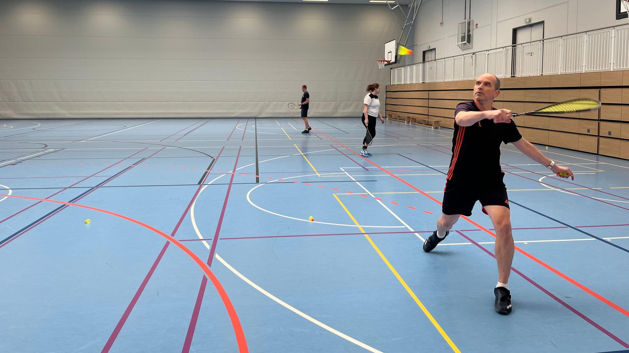 Ein Mann spielt Crossminton in einer Sporthalle.