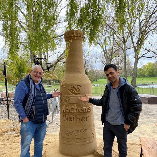 Josef Rayes (l.), der Betreiber des Biergartens und Yosef Bakir Sandkünstler vor der Flasche des Aachener Weihers.