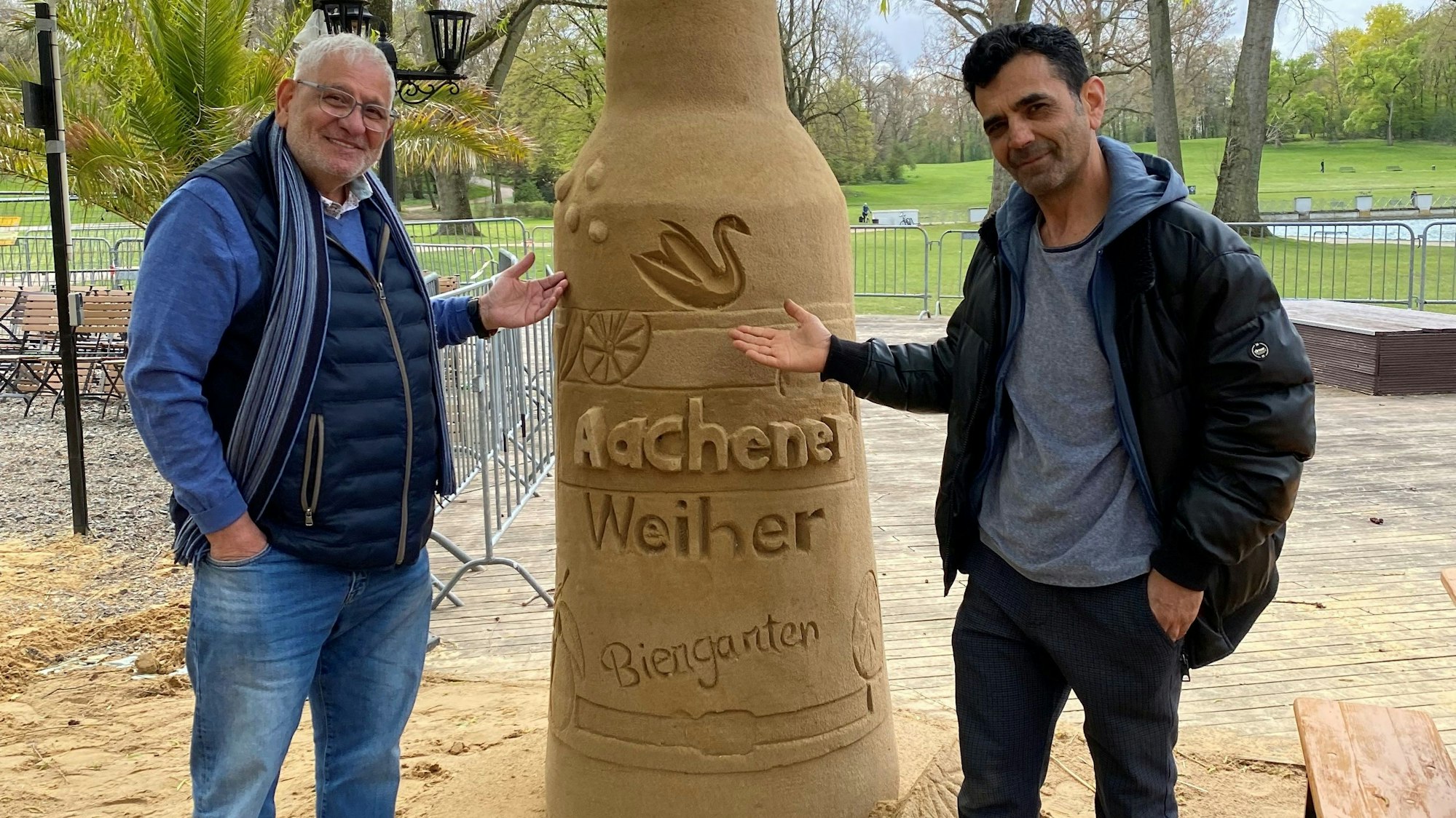 Josef Rayes (l.), der Betreiber des Biergartens und Yosef Bakir Sandkünstler vor der Flasche des Aachener Weihers.