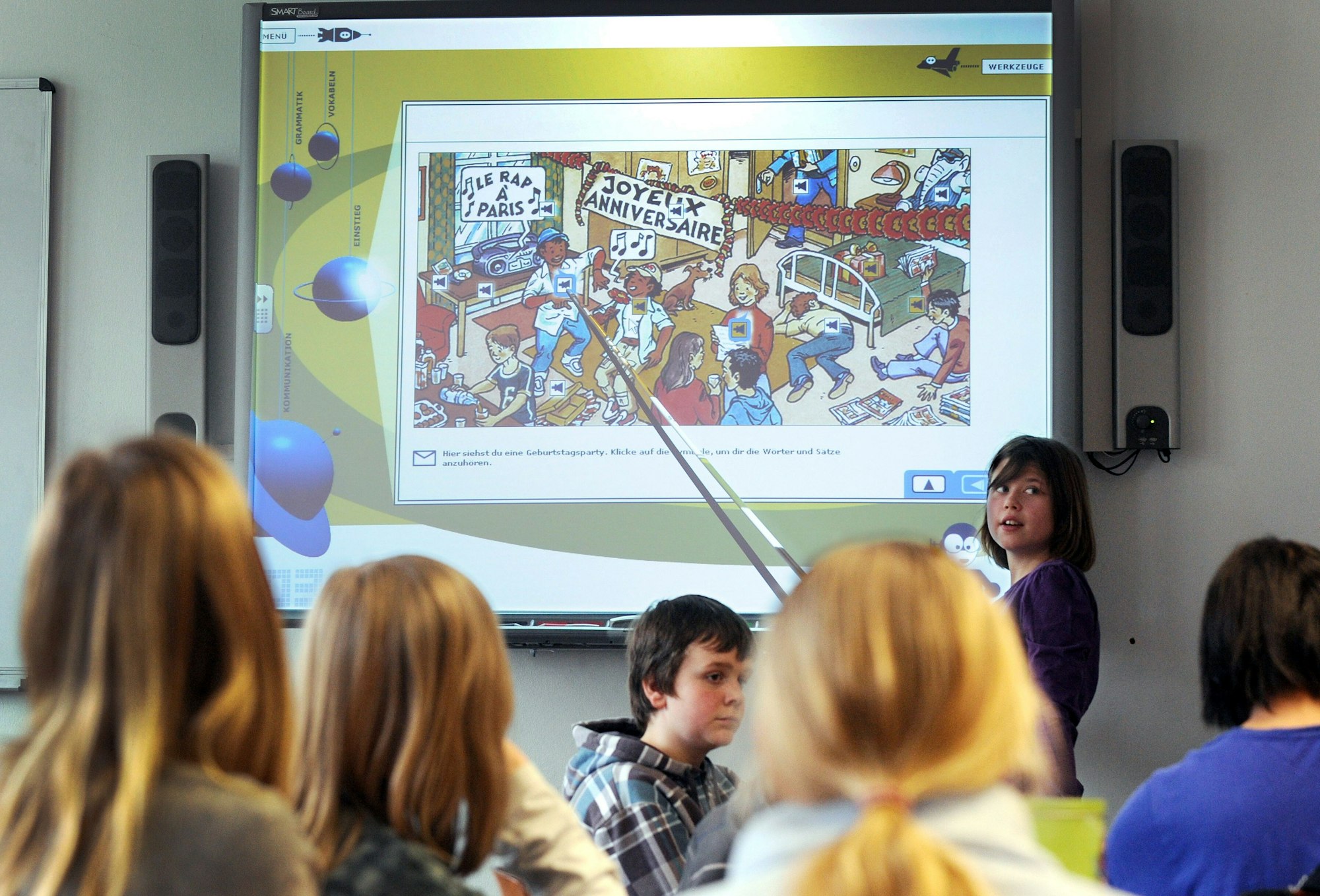 Eine Schulklasse schaut auf eine digitale Tafel mit einer bunten Zeichnung