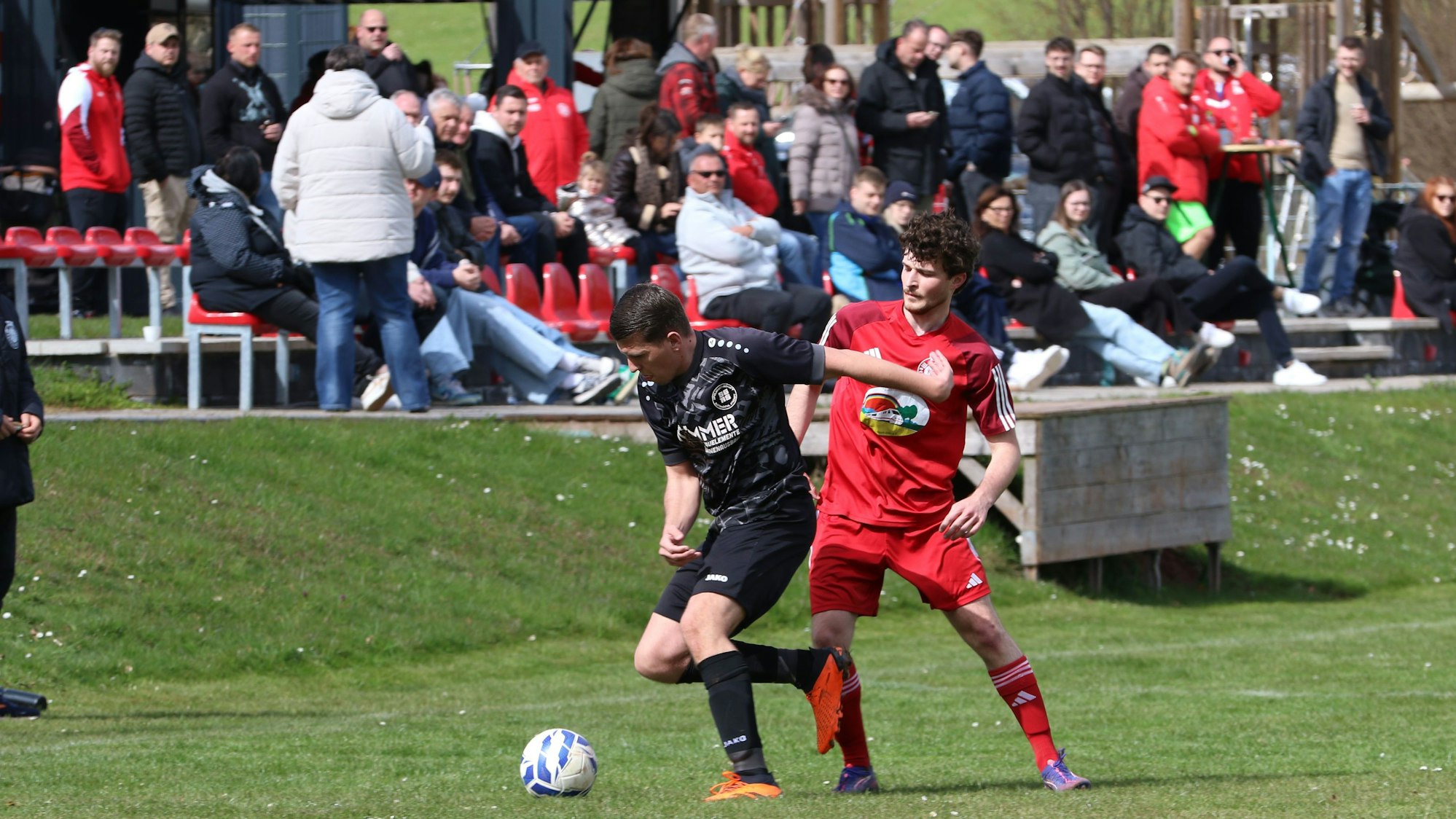 Simon Dürbaum (l.) wird von Mechernichs Marcel Zahn bedrängt. Im Hintergrund ist das Publikum zu sehen, das in der Sonne sitzt.