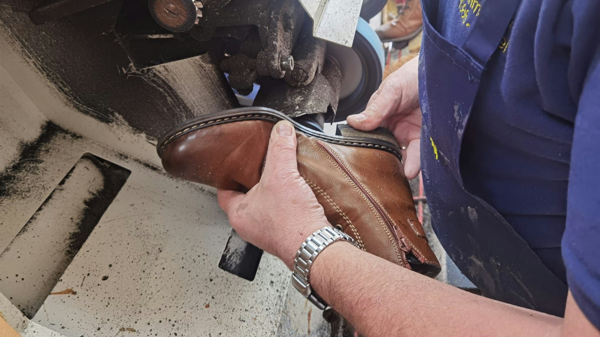 Ein Lederschuh wird an eine Maschine gehalten, die seine Sohle schleift.