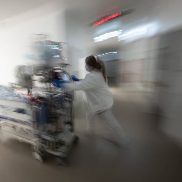 Eine Pflegerin fährt eine Intensivpatientin in einem Krankenbett durch einen Gang einer Klinik.