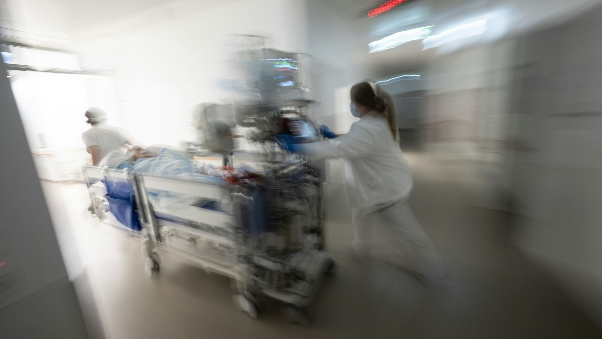 Eine Pflegerin fährt eine Intensivpatientin in einem Krankenbett durch einen Gang einer Klinik.