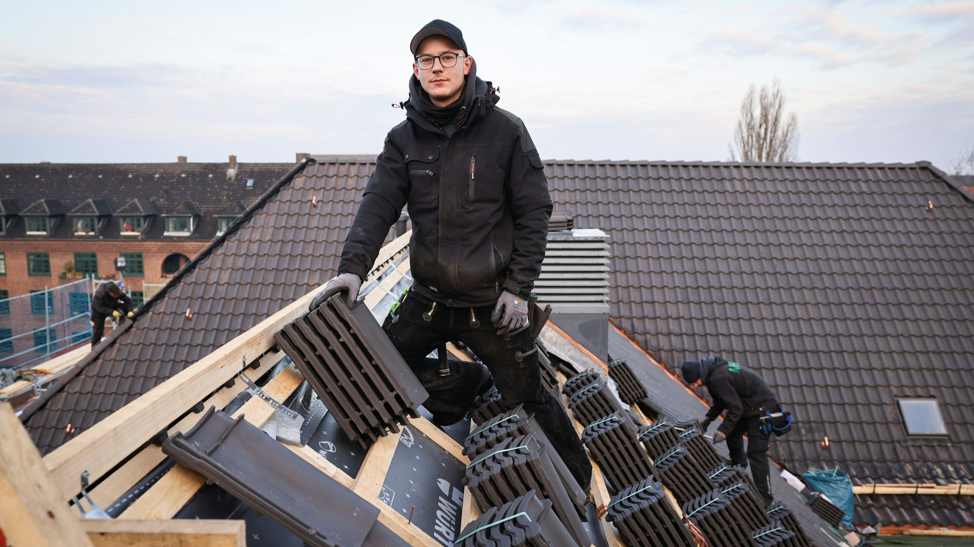Tim Hoppe, Dachdeckermeister, und seine Kollegen arbeiten auf der Dachfläche eines Schulgebäudes.