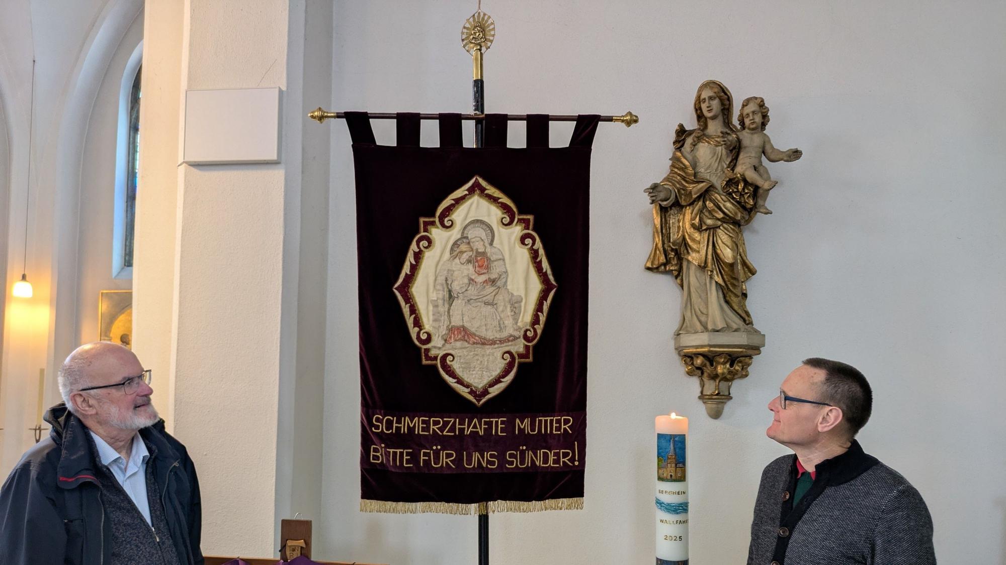 Zwei Männer stehen vor einer Pilgerfahne.