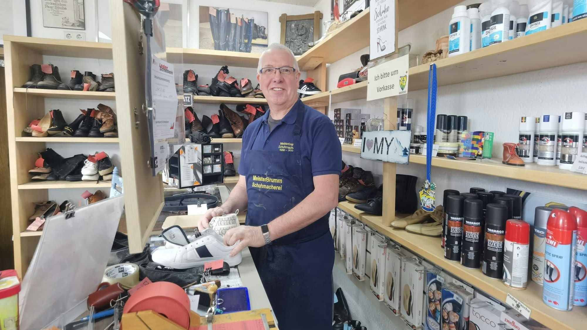 Ein Mann steht hinter dem Tresen einer Schuhmacherei und lächelt.