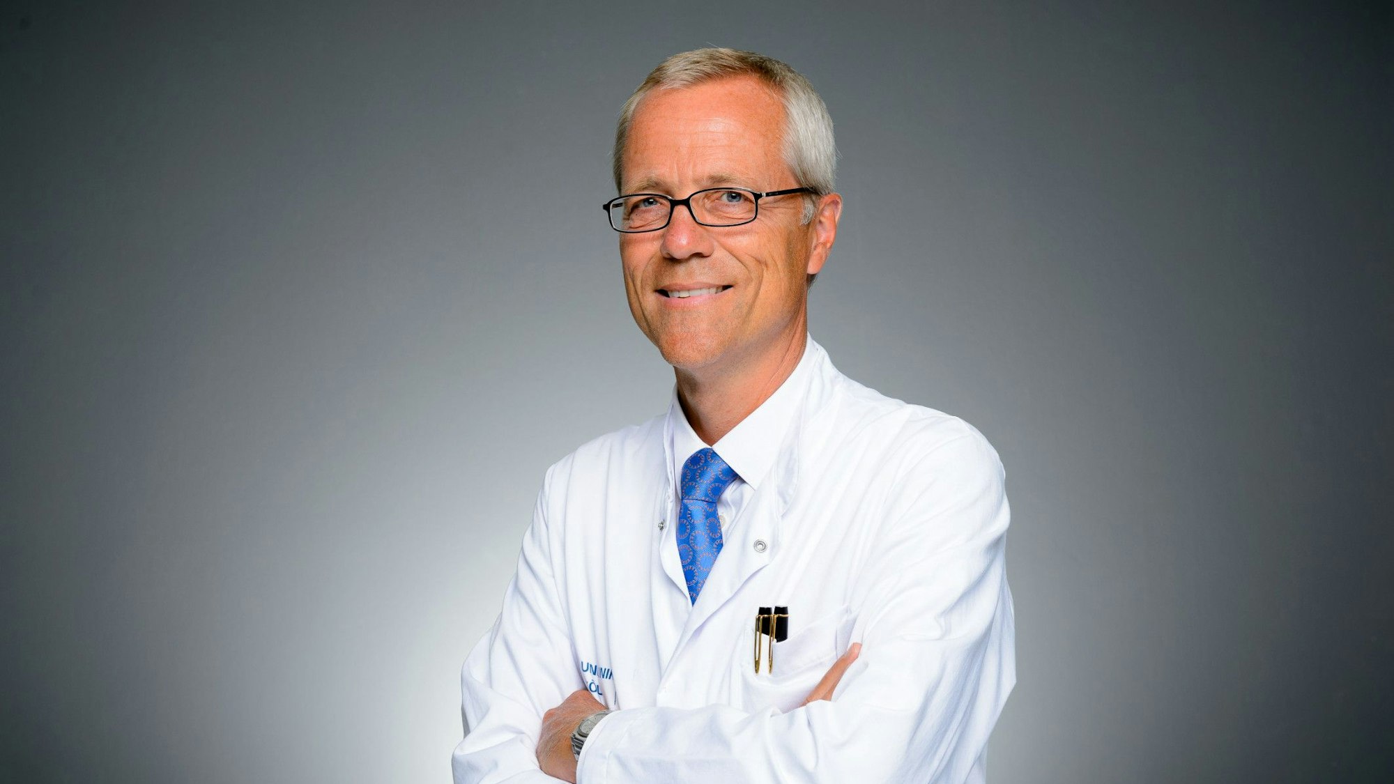 Ein Mann im weißen Kittel mit Krawatte lächelt in die Kamera