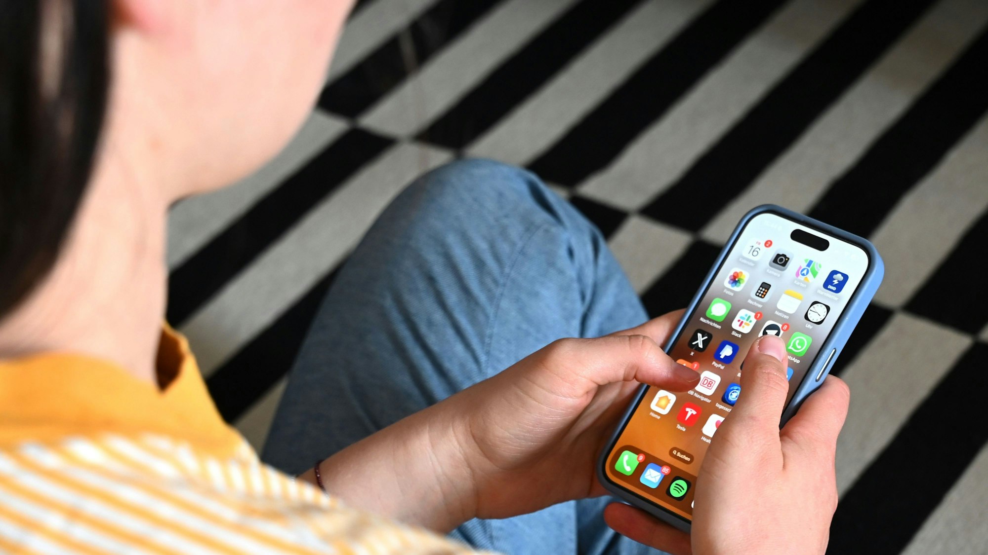 Eine Jugendliche sitzt auf dem Boden und nutzt ein Smartphone.