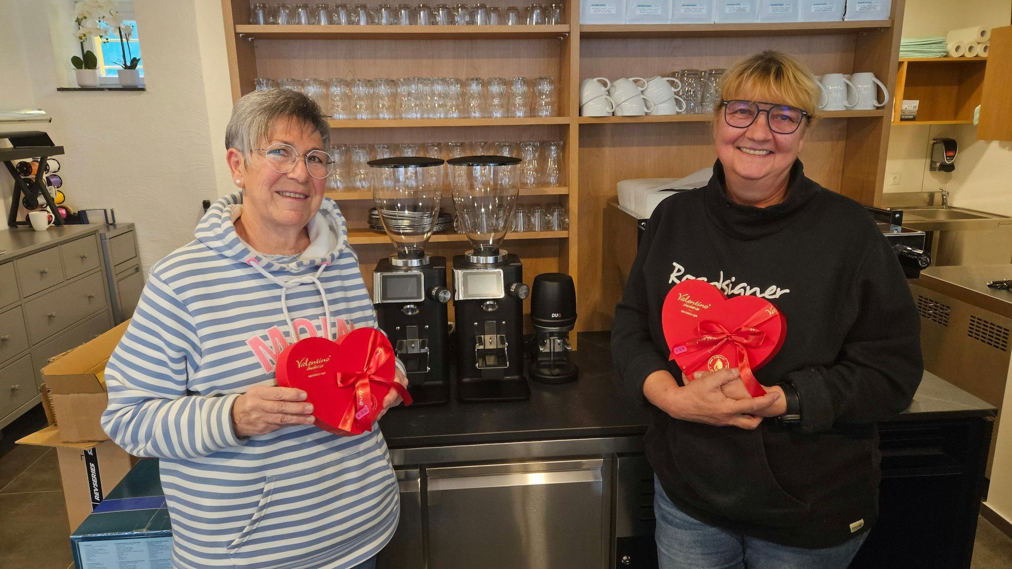 Zwei Frauen stehen nebeneinander und präsentieren Verpackungen in Form von roten Herzen.